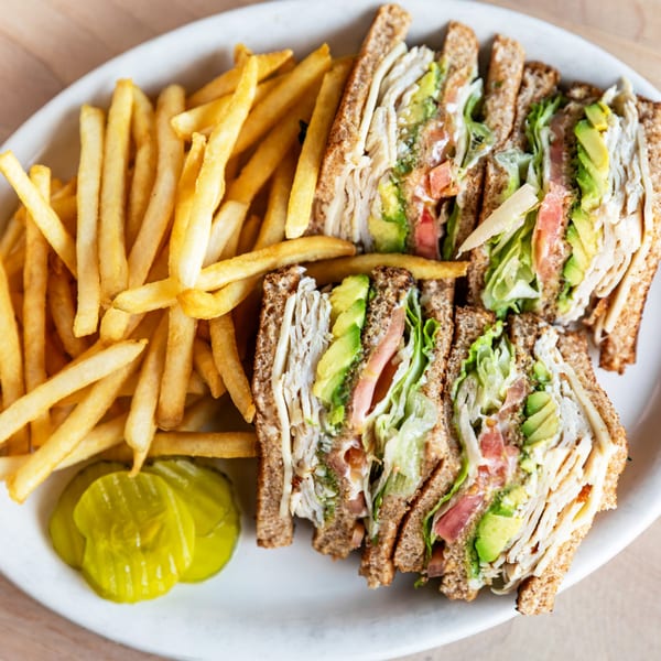 Cornerstone Cafe & Bar's turkey club sandwich with avocado, lettuce, tomato, and a side of fries and pickles.