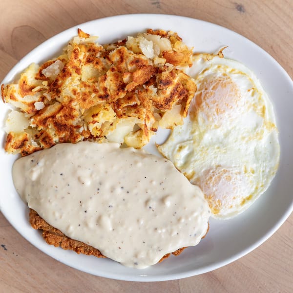 Chicken fried steak with gravy, hash browns, and two fried eggs on a white plate.