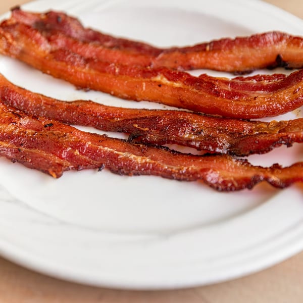Four crispy strips of bacon, perfectly cooked, resting on a white plate at Cornerstone Cafe & Bar.