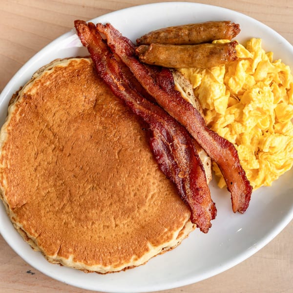 A Cornerstone Cafe & Bar breakfast plate with pancakes, crispy bacon, sausage links, and scrambled eggs.