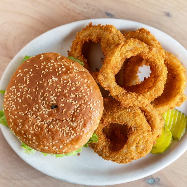 A sesame seed bun burger with lettuce, served with crispy onion rings and pickle slices.