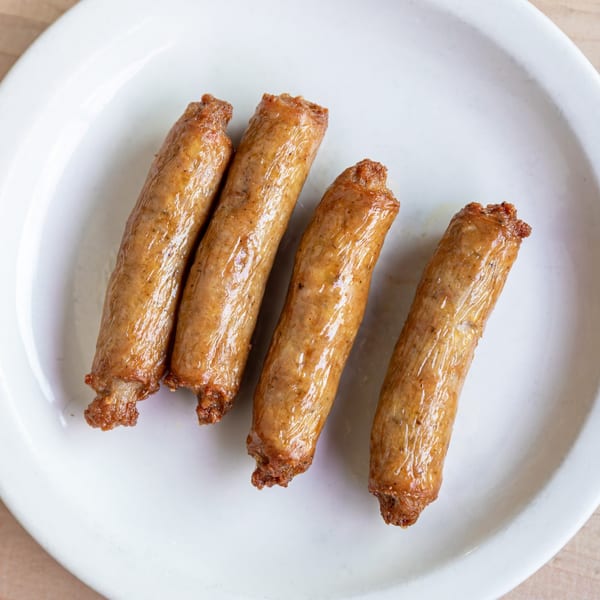 Four breakfast sausage links, golden brown and glistening, arranged on a white plate.