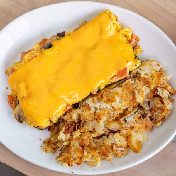 A Cornerstone Cafe & Bar omelet with melted cheese, mushrooms, and hash browns on a white plate.